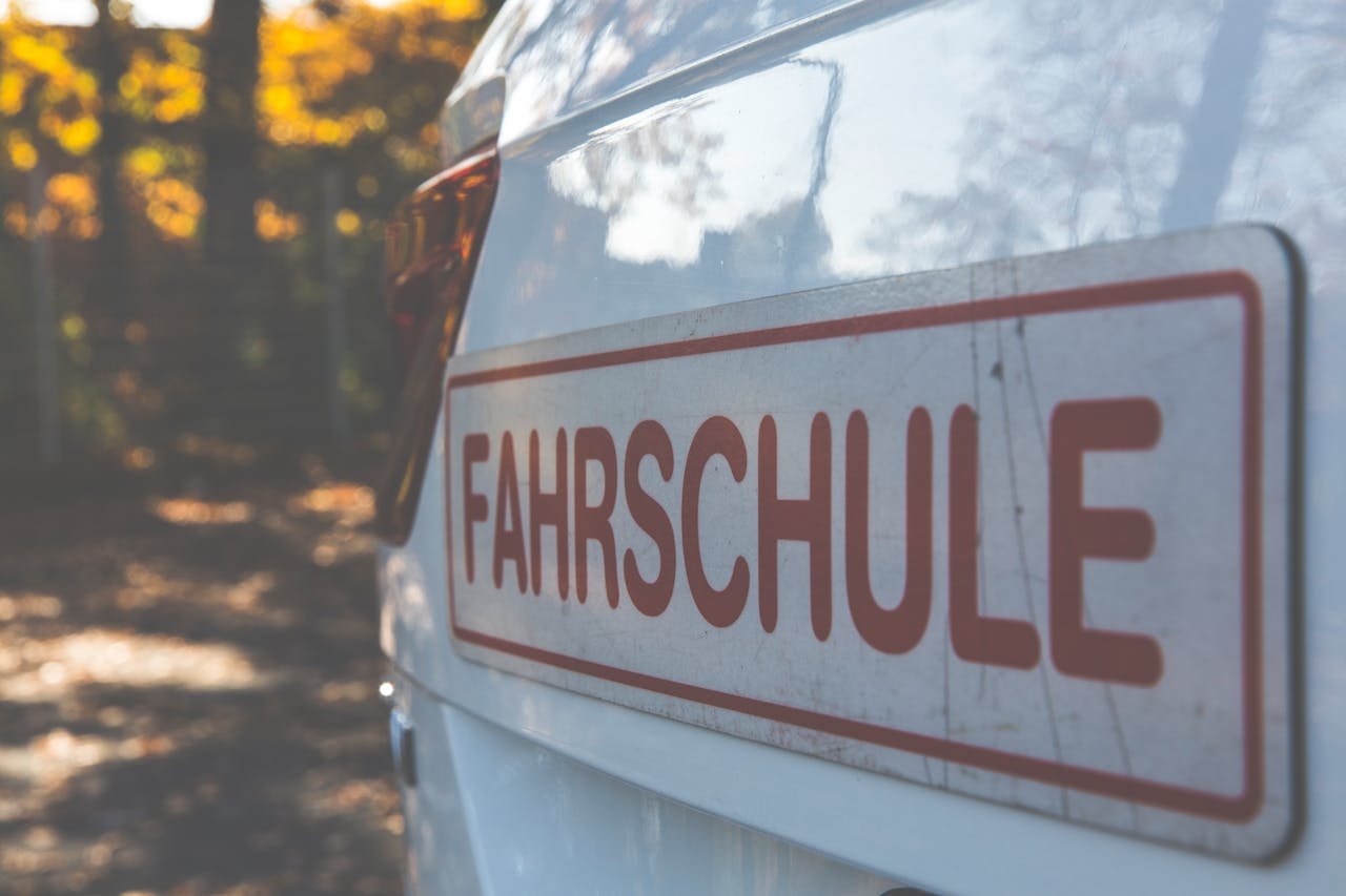 Services A side view of a white car with a Fahrschule sign, outdoors with autumn foliage.
