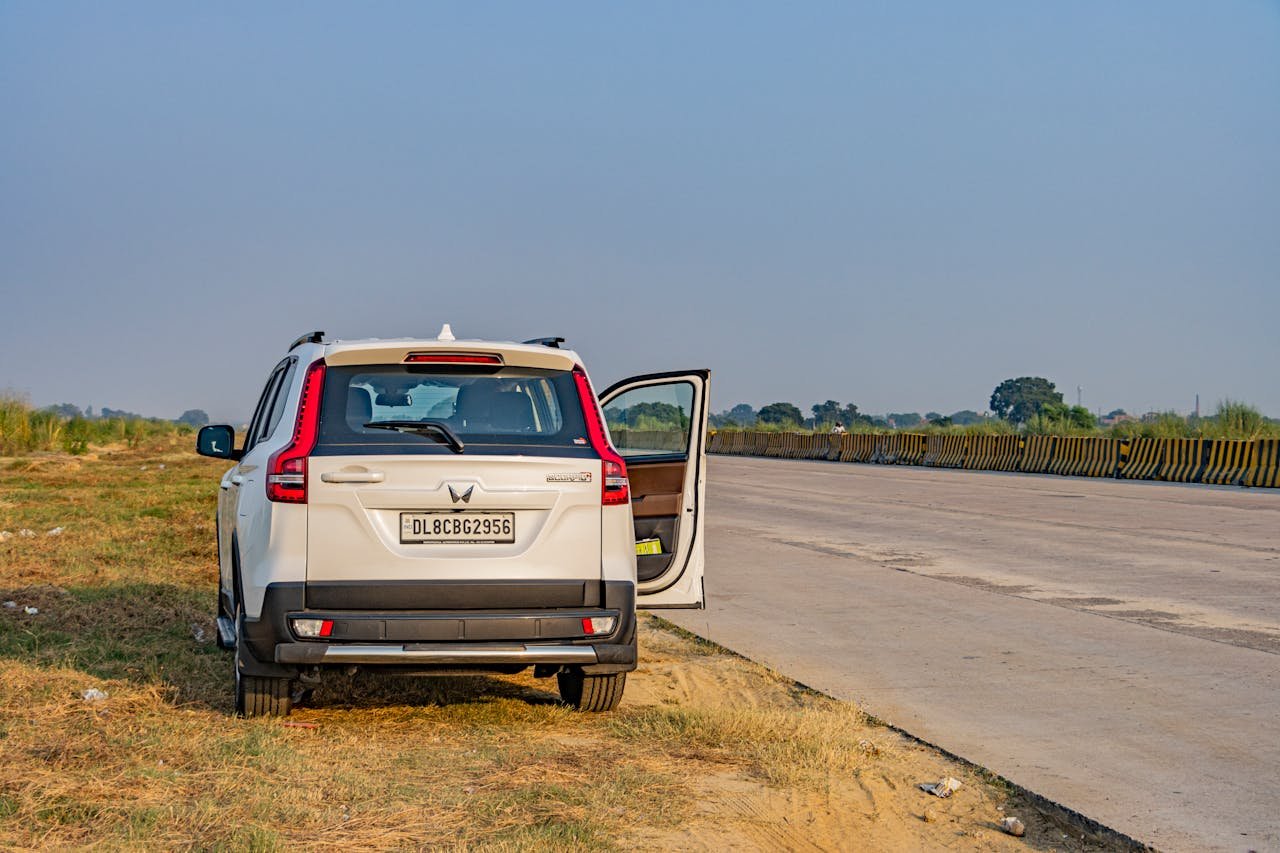 Services A white SUV parked on a deserted Indian highway during daytime, capturing the vast open road and landscape.