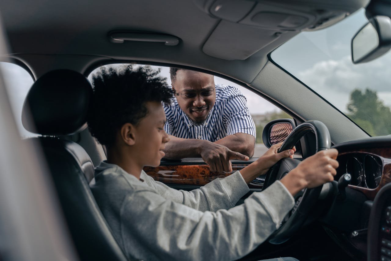 The Art of Drawing Readers In: Your attractive post title goes here Young boy sitting at the wheel while father instructs from outside, learning to drive.